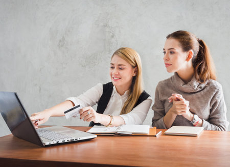 Two of young caucasian business woman working with happy feeling and smile in the office, sitting on desk with computer laptop reading good news and feeling surprise.の写真素材