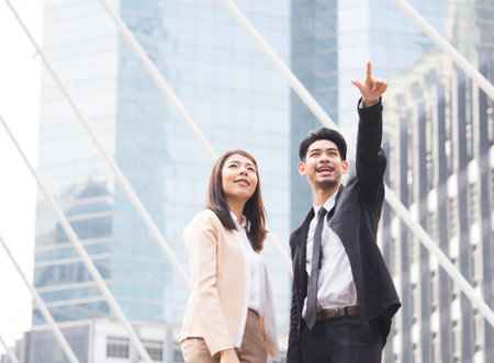 two of young asian businessman businesswoman 20-30s standing in the modern city, pointing out showing business plan in the futureの写真素材