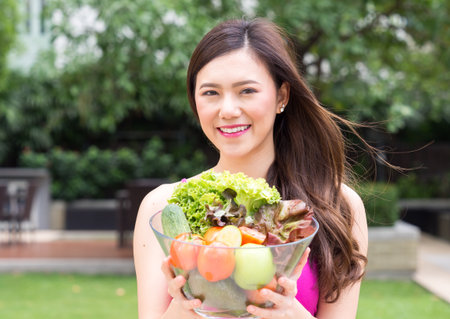 Young beautiful asian woman eating fresh clean food with tomato vegetables and fruits for good healthy over green background, healthy food woman for dietの写真素材