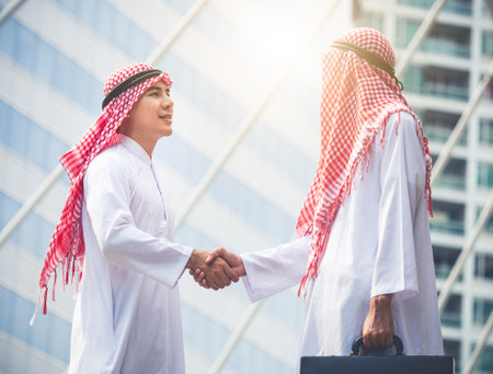 Handsome arab businessman, engineer/architect shaking hands front of building new construction project, togetherness, teamwork, cooperation for business conceptの写真素材