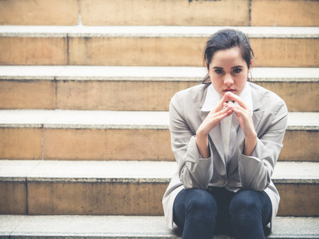 Upset young caucasian beautiful businesswoman tired from work sitting at stairs, unemployment, fired from job, disappointed, loss and feeling down conceptの写真素材