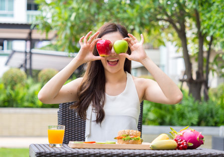 Young beautiful asian woman eating fresh clean food with vegetables red/greed apples fruits for good healthy over green background, healthy food woman for dietの写真素材