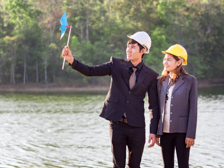 Asian engineer holding pin wheel over the nature river in forest, energy saving, wind mill conceptの写真素材