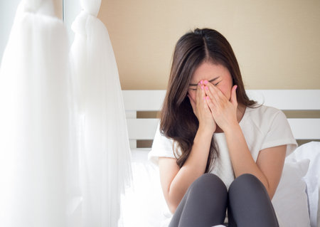 Young beautiful asian woman headache on white bed, sad, stressed, crying, disappointed feeling in the morningの写真素材