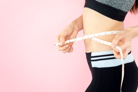 Young asian beautiful woman with sport fitness concept, workout, exercise, measure tape at waist on pink backgroundの写真素材