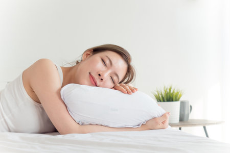 Young beautiful asian woman sleeping happy on white bed with happy feelingの写真素材