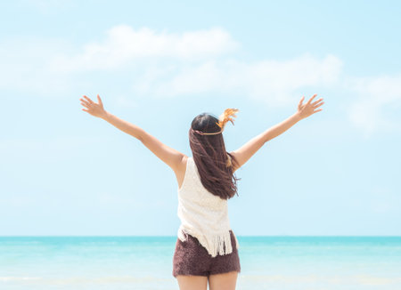 Happy young woman rising hands to sky at sea/beautiful beach, freedom, relaxing on vacation/holiday.の写真素材