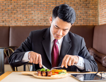 Young asian businessman in formal suit feeling hungry, eating many foods on table at cafeの写真素材