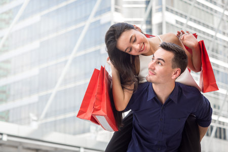 Woman on man's back holding shopping bags with happy feeling, couple shopping conceptの写真素材