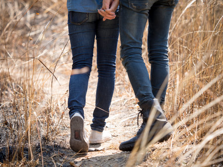 Two young couple wears jeans holding hands in meadow, hipster looking, walking to travel in mountain for trekking/hiking/camping on holiday/vacation/backpacking, freedom lifestyle for teenager conceptの写真素材