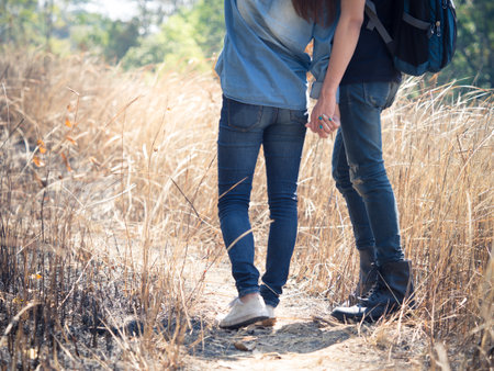 Two young couple wears jeans holding hands in meadow, hipster looking, walking to travel in mountain for trekking/hiking/camping on holiday/vacation/backpacking, freedom lifestyle for teenager conceptの写真素材