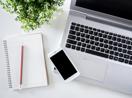 Top view of white working table in office for business man/women with laptop, notebook, pencil and smart phone(isolate black screen) in white tone creative design.の写真素材