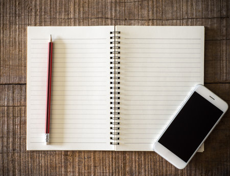 Close up vintage old notebook, pencil and smart phone isolated screen on wooden backgroundの写真素材