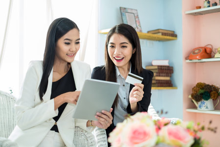 Two young asian businesswoman in suit using tablet and credit card for online shopping, internet...