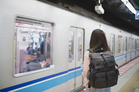 Back side of Asian woman backpacker waiting for train station during travel on holiday in Japan