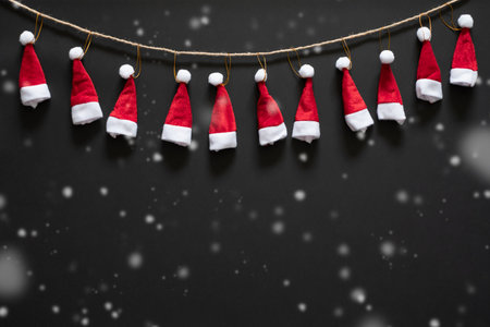 Christmas background with red santa hats and snow over black background and copy space. flatlayの写真素材