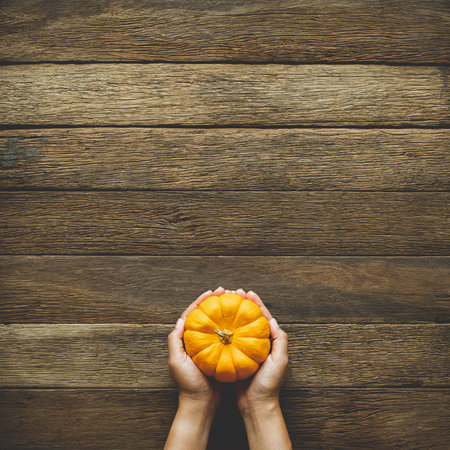 Thanksgiving background, human hand holding pumpkin over wood table background with copy space. flatlayの写真素材