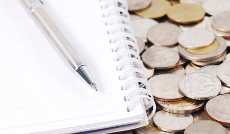 silver pen on notebook with coins backgroundの写真素材