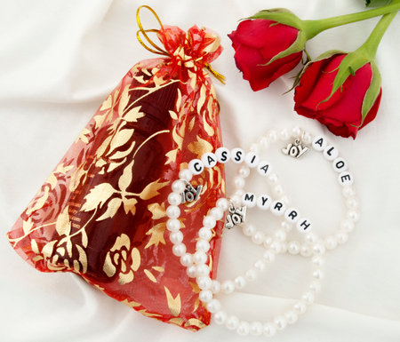 Small bottle of Anointing Oil in Gift Bag, Three Pearl Bracelets and Two Red Roses on White Backgroundの写真素材