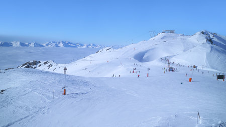 Skiers and snowboarders on snowy piste in skiing resort of Les Trois Vallees, Alps, France, with white mountains peaks above the low clouds in the valley .の写真素材