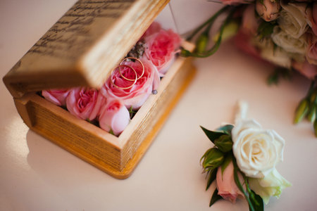 wooden flower box with gold wedding rings and pink roses on a white surfaceの写真素材