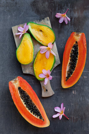Overhead still life of fresh and juicy tropical fruits on a dark shabby background. Vegan food:...