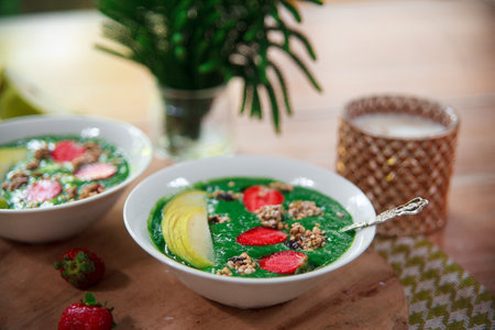 Healthy vegan food concept: green smoothie bowl with spinach, spirulina, pear and red strawberry topped with raw superfood granola. Vegetarian bright breakfast.の写真素材