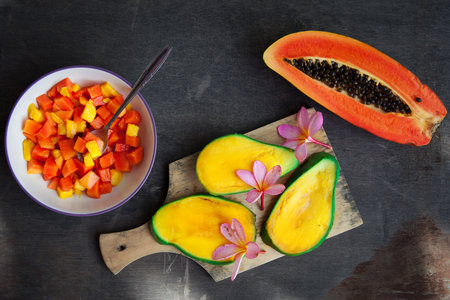 Healthy vegan breakfast of raw tropical fruits. A bowl of sliced fresh mango, papaya, plumeria...