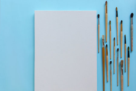 Textured blank white canvas and a lot of different sizes brushes for painting on pastel blue paper background with copy space. Drawing education for beginners and inspiration concept.の写真素材
