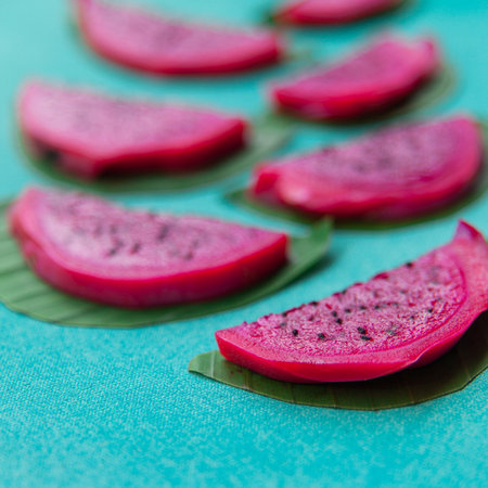 Colorful overhead still life of red dragon fruit slices on a bright blue textured background with green leaves. Vegan healthy food concept. Contrast tropical fruit.の写真素材