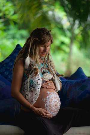 Caucasian pregnant woman with dreadlocks in boho style. White mehendi on big belly. Expectation of baby in new age lifestyle. Conscious parents concept.の写真素材