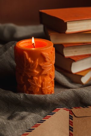 Autumn cozy still life of big orange candle and pile of books with warm scurf.の写真素材