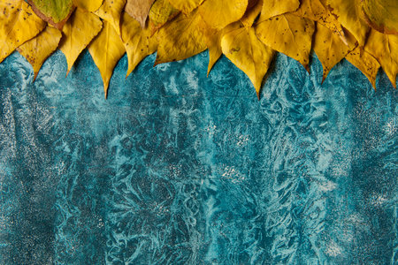 Autumn yellow leaves background. Bright foliage border on textured blue surface. Fall season copy space.の写真素材