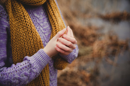 Fall sadness background. Unrecognisible girl in lilac knitted sweater and ocher scarf warming her hands close up.の写真素材