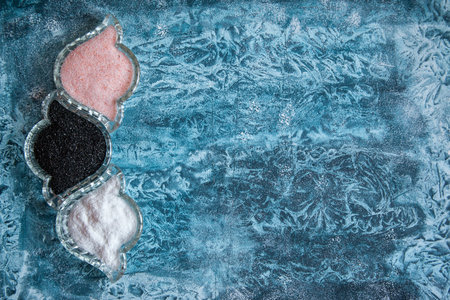 Flat lay border of three different colors of salt: pink, black and white on bright blue background.の写真素材