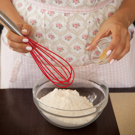 Plump woman mixes dry ingredients for baking, using red silicone whisk in a glass bowl. Home cooking on the kitchen.の写真素材