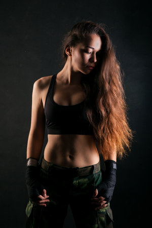 Athletic girl with long hair, wearing sport top, standing on black studio background.の写真素材