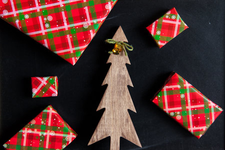 Flat lay with wrapped gift boxes and a wooden figure of a Christmas tree on a black chalk board.の写真素材