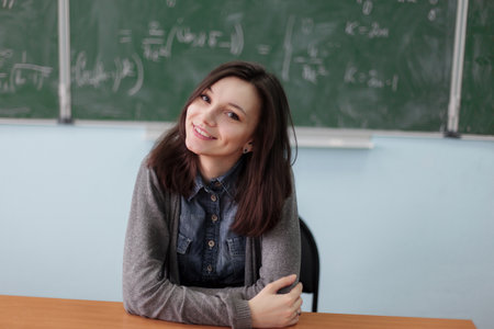 Smart pretty girl sitting in college classroom on background of green chalkboard with high math formulas. Higher education concept.の写真素材