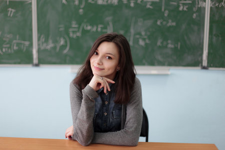 Smart pretty girl sitting in college classroom on background of green chalkboard with high math formulas. Higher education concept.の写真素材