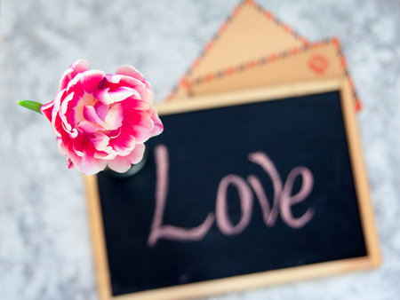Pink tulip in glass bottle and vintage kraft envelopes with kiss print on background of black chalkboard with inscription love.の写真素材