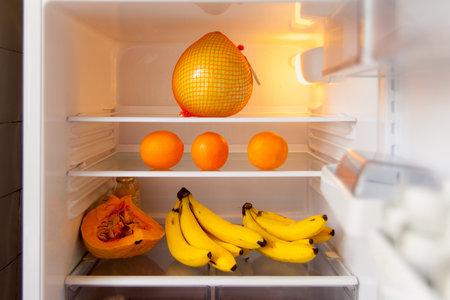 Open fridge with orange and yellow fruit inside on white shelves. The concept of a healthy diet.の写真素材