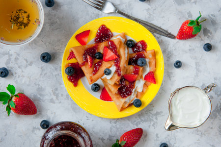 Two thin pancakes, folded in triangles, are poured with sour cream, jam and decorated with fresh berries. The concept of Russian holiday Maslenitsaの写真素材
