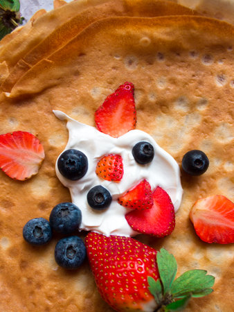Overhead stack of thin pancakes poured with sour cream and decorated with fresh strawberries and blueberries. The concept of Russian holiday Maslenitsa, Shrovetide.の写真素材