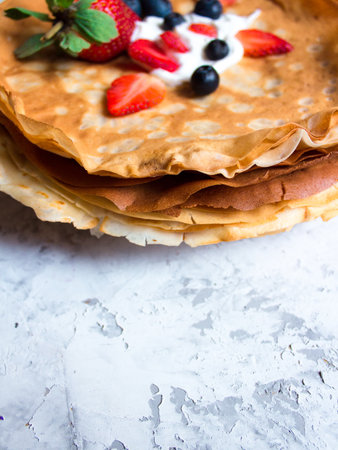 Side view of stack of thin pancakes poured with sour cream and decorated with fresh strawberries and blueberries. The concept of Russian holiday Maslenitsa, Shrovetide.の写真素材
