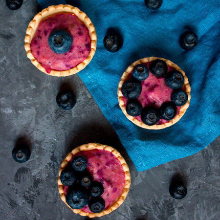 Sweet mini tartlets with cream and berries on a blue linen cloth. Simple dessert snack recipe with...