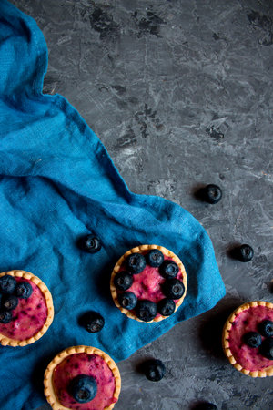 Sweet mini tartlets with cream and berries on a blue linen cloth. Simple dessert snack recipe with blueberry. Summer food conceptの写真素材