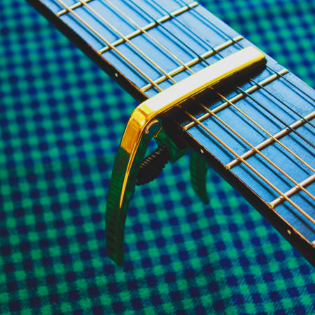 Golden capo on acoustic guitar neck on cozy plaid textile background. Musical instrument equipmentの写真素材