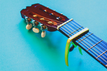 Golden capo on acoustic guitar neck on blue background. Musical instrument equipment. Simple music conceptの写真素材