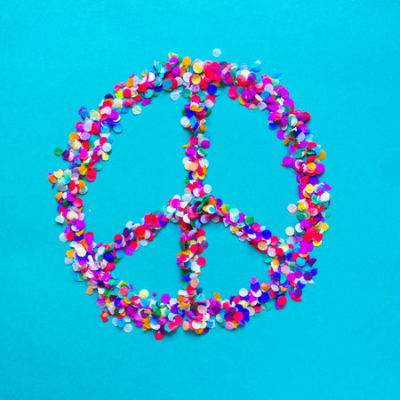 Hippie sign made of colorful confetti on blue background. Bright peace symbol